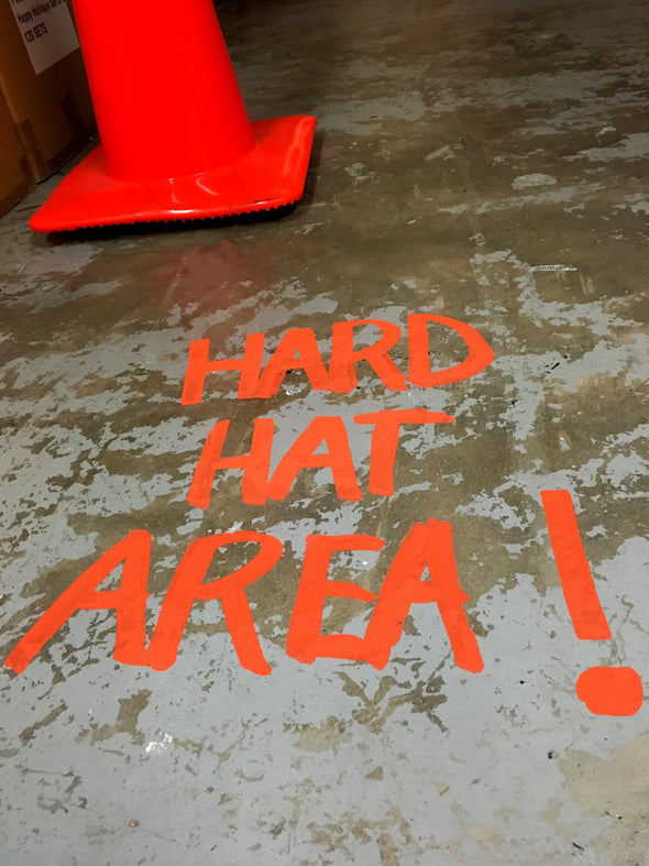 Warehouse floor with orange caution cone and the words Hard Hat Area written on the floor in Chalk Ink Safety Marker caution orange ink