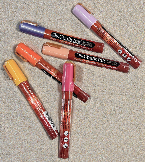 Product image of chalk ink liquid chalk markers in sunset inspired colors laying on beach sand