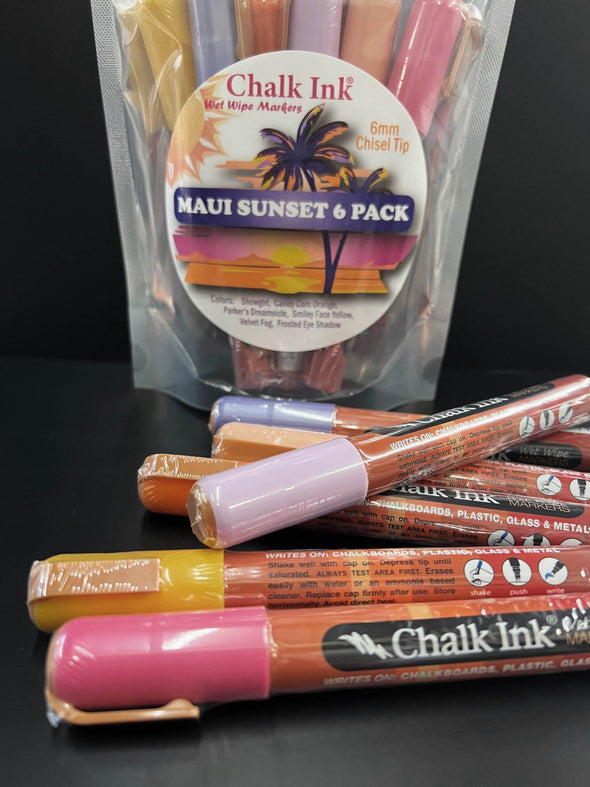 Closeup of chalk ink liquid chalk variety pack of markers on a black table in front of chalk ink Maui Sunset packaging