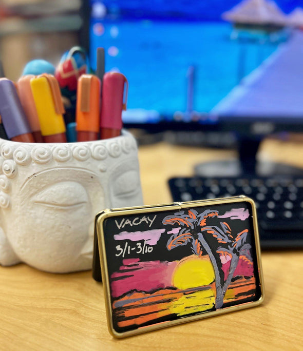 Image of countertop mini chalkboard with a drawing of a sunset and the words vacay written on it using chalk ink liquid chalk markers in sunset colors