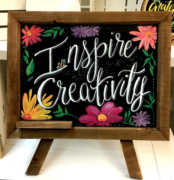 Image of a wood framed black chalkboard with the words inspire creativity and colorful flowers drawn on it using chalk ink liquid chalk markers